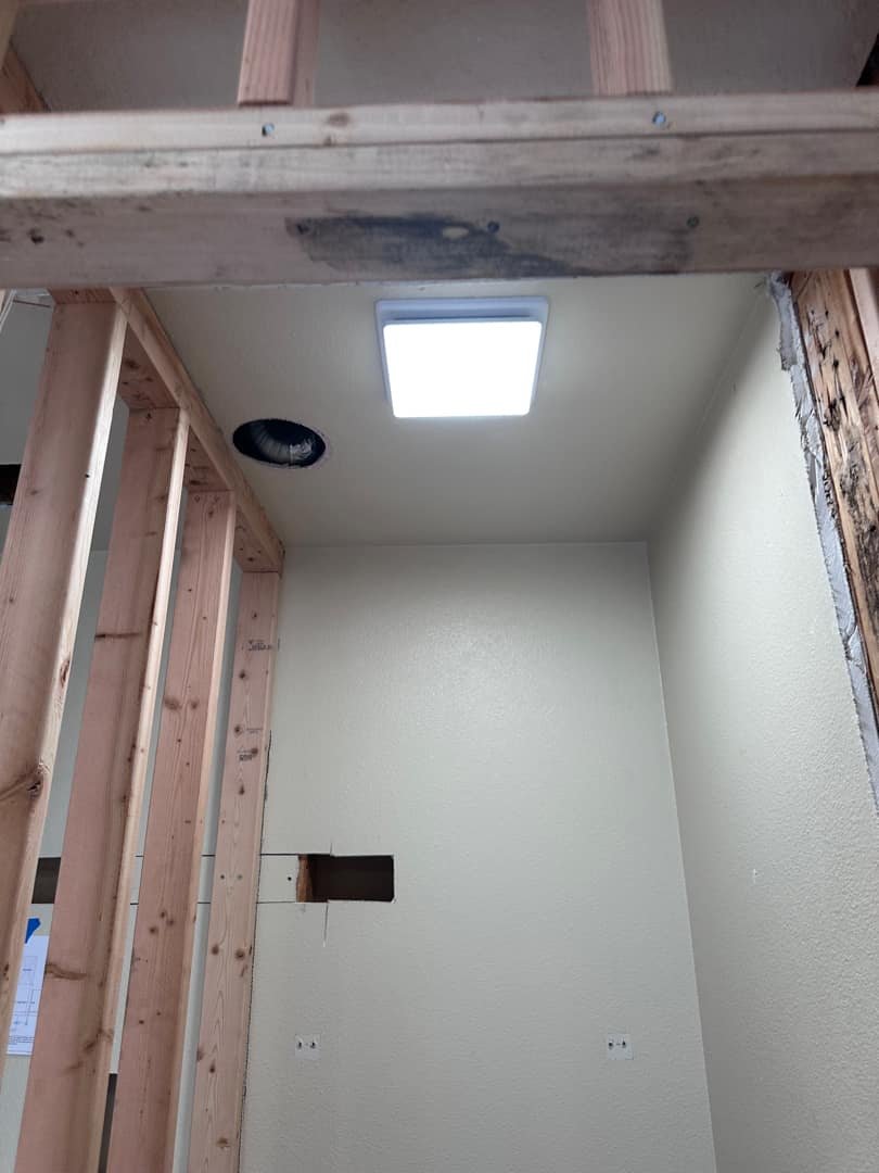 Square LED ceiling light fixture installed in unfinished drywall and framing.