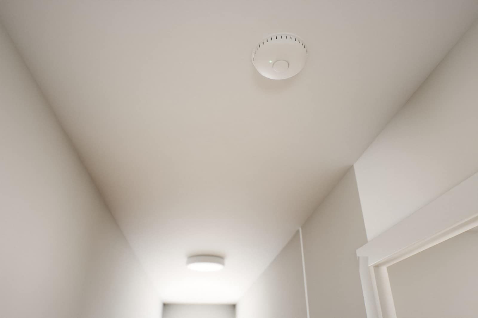 Smoke alarm on a hallway ceiling just outside a bedroom doorway