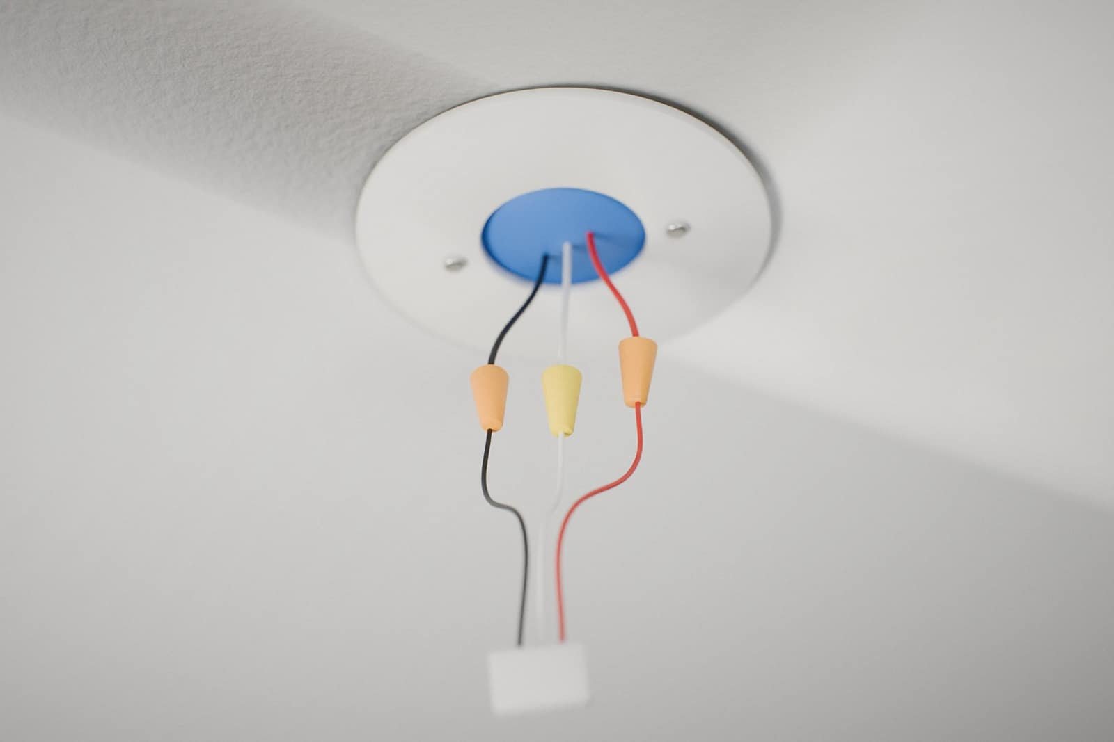 Hardwired smoke alarm wiring at a ceiling box: black, white and red wires joined with wire nuts to the alarm's plug-in harness