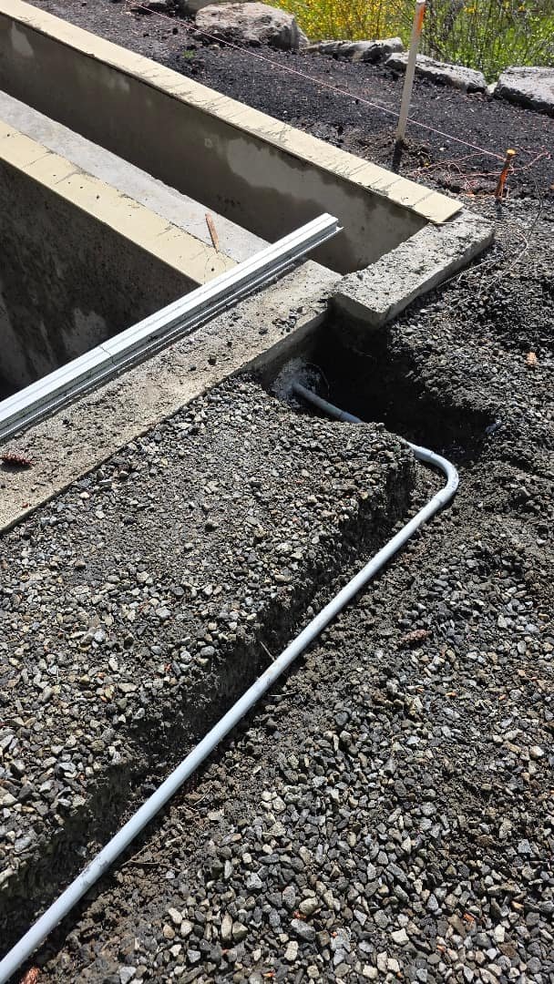 Electrical conduit being installed in a trench alongside prepared concrete forms.