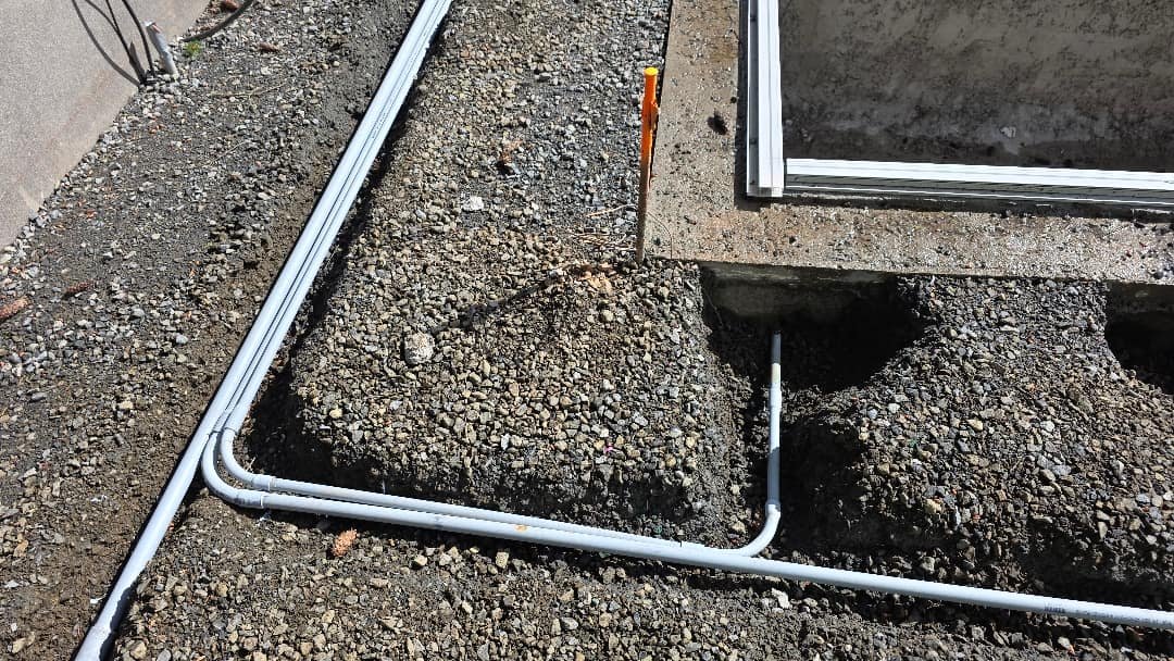 Electrical conduit installation visible along the ground, leading to a concrete structure with exposed gravel and soil.