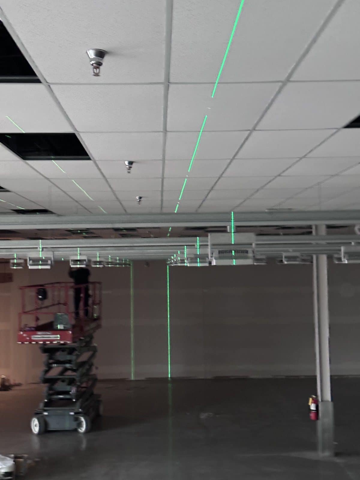 Green laser layout lines projected across a new ceiling grid to set fixture and device locations before the lighting package went in