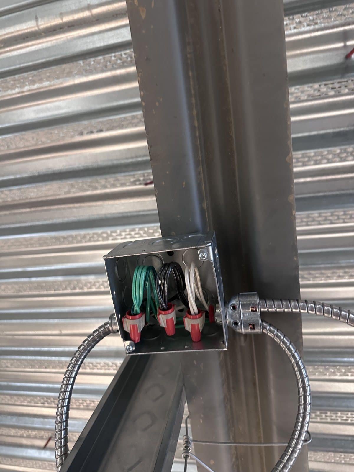 Four-inch square junction box mounted to a structural steel beam above the deck, with MC cable connectors and made-up branch circuit conductors