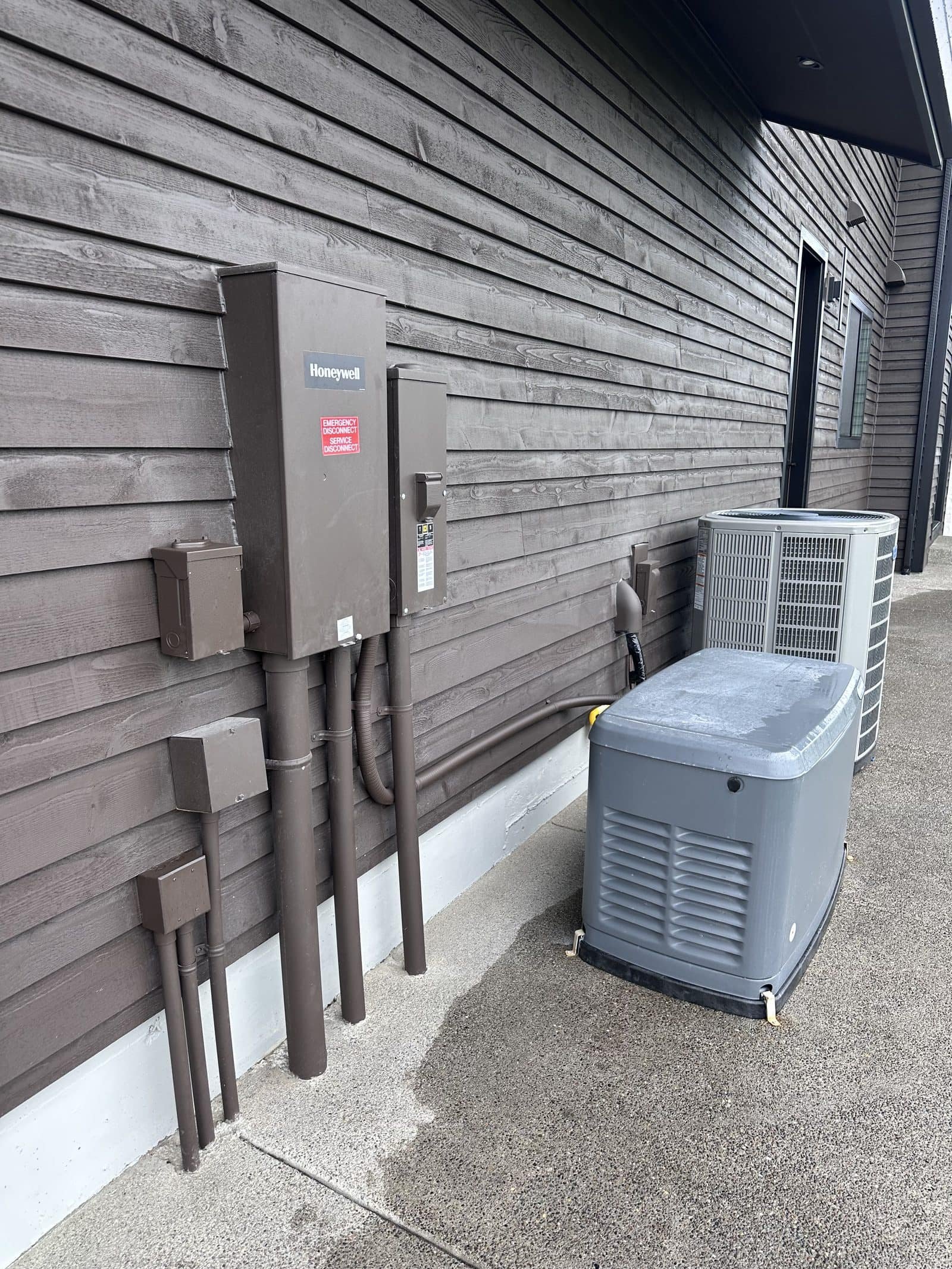 22 kW Honeywell home standby generator next to the heat pump condenser, with the automatic transfer switch and color-matched conduit on the cedar siding